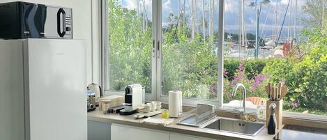 A modern kitchen with a built-in dishwasher, a large window offering a view of boats and greenery.