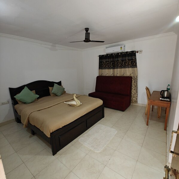 A bedroom with a bed, a chair, a table, and a ceiling fan. - Nisarga Resort (Bengaluru)