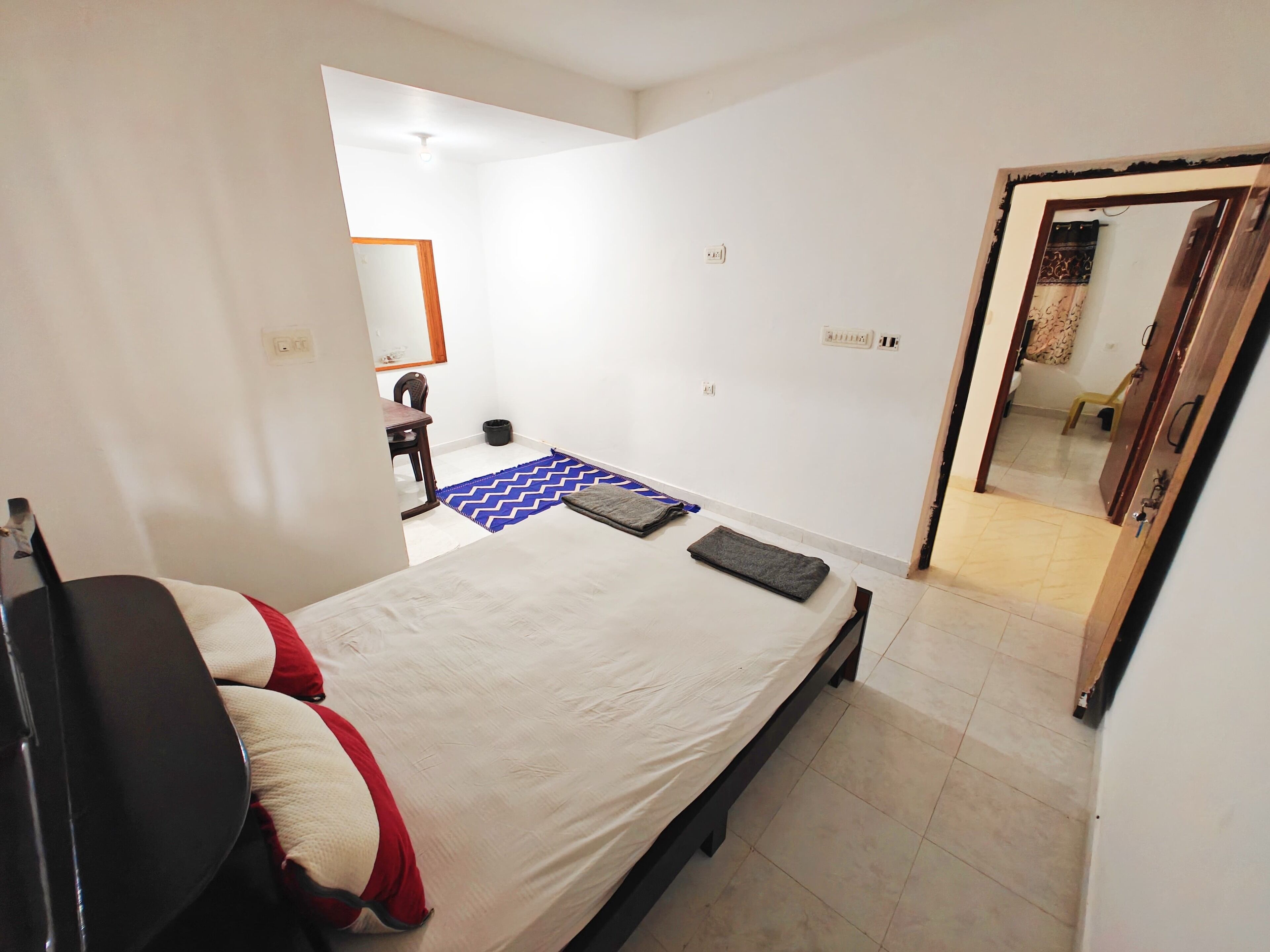 A bedroom with a bed, a chair, a desk, and a mirror.