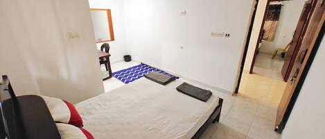 A bedroom with a bed, a chair, a desk, and a mirror.