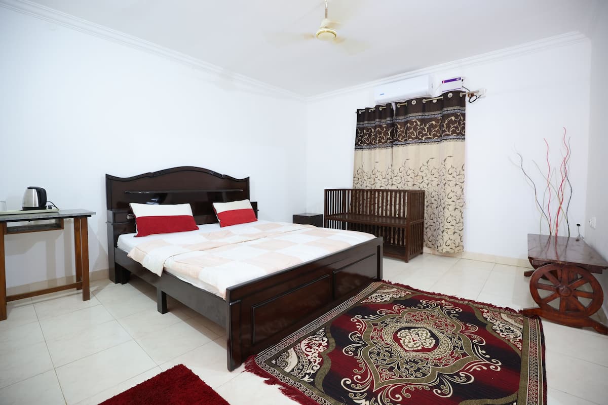 A bedroom with a bed, a desk, a chair, a rug, and a window with curtains.
