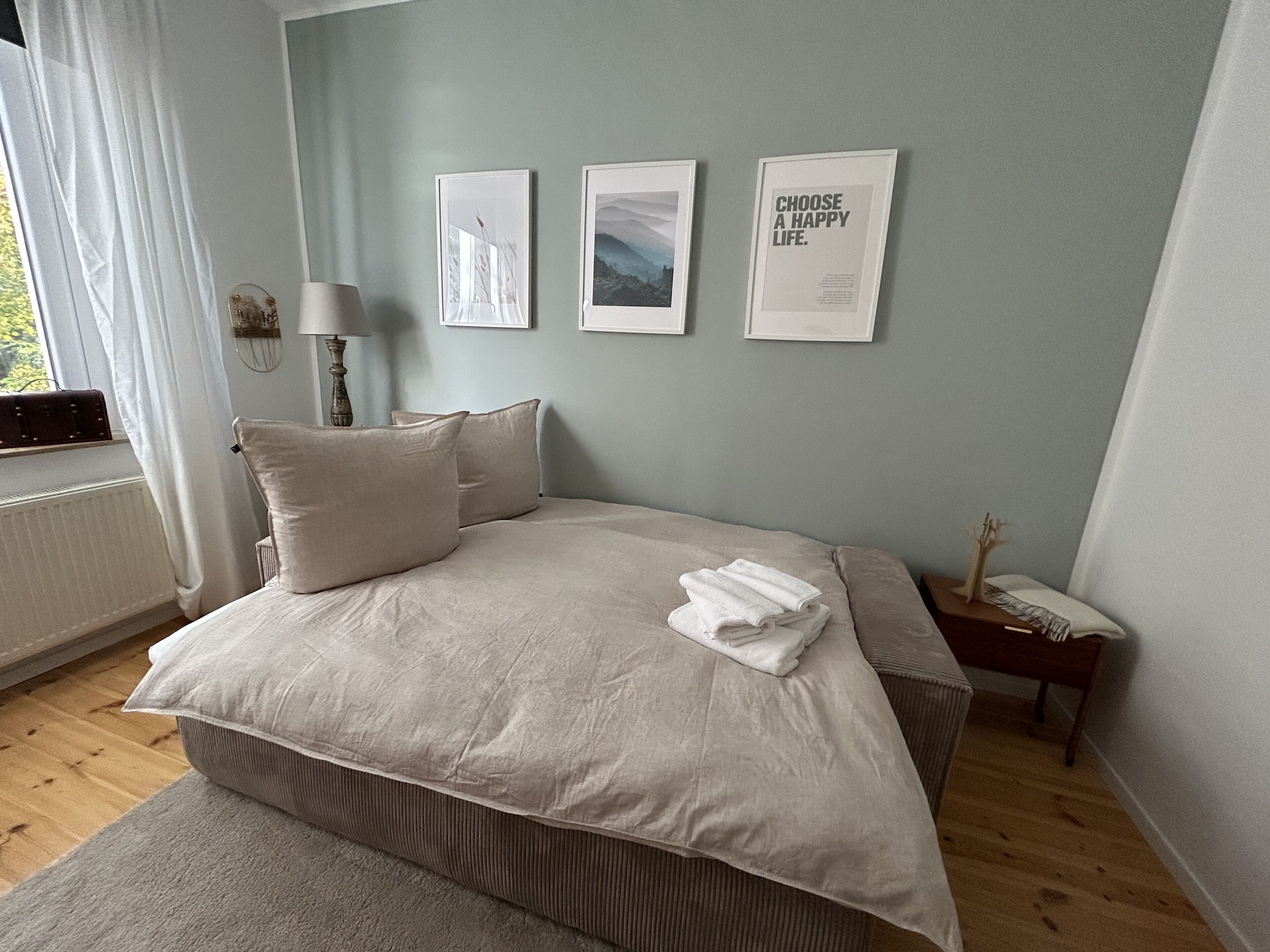 Ein Schlafzimmer mit Bett, Kissen, einem Nachttisch, einer Lampe und gerahmten Bildern an der Wand.