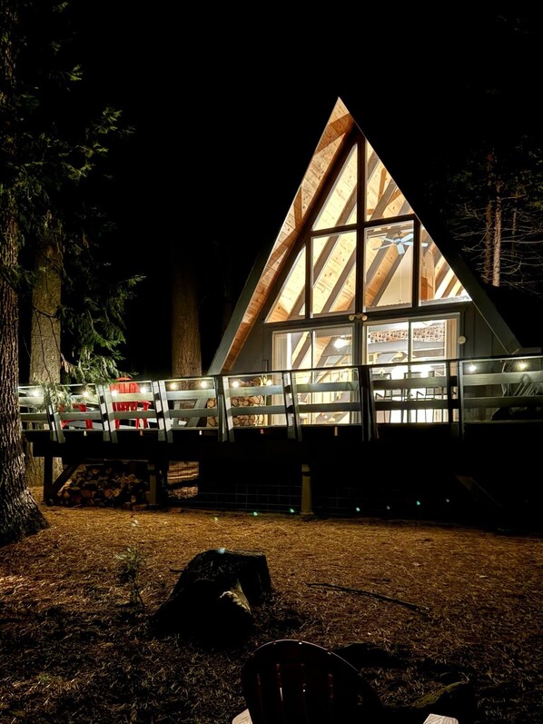 Una cabaña de madera triangular con fachada de vidrio, una terraza cubierta y un banco.