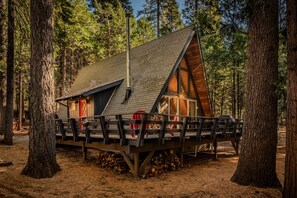 Una cabaña con terraza de madera, techo inclinado y un ventanal grande.