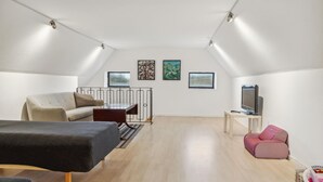 Ein modernes, helles Schlafzimmer im Dachgeschoss mit einem Hochbett, einer Couch, einem Fernseher und Bildern an den Wänden.