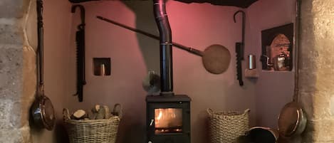 A traditional fireplace with a log basket, a cat, and a rustic interior.