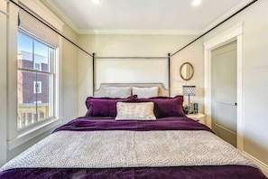 Une chambre à coucher avec un lit, une fenêtre, une table de chevet avec une lampe et une porte.