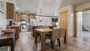 Une cuisine moderne avec des meubles en bois, des appareils en acier inoxydable et un coin repas comprenant une table et des chaises en bois.