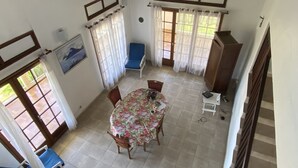 A dining area with a round table, chairs, and a blue sofa. - Location Saisonnière Grand Espace Familial. Plage, Activités Nautiques à 5 mn (Le Moule)