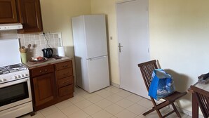 A kitchen with a stove, oven, refrigerator, and wooden cabinets. - Location Saisonnière Grand Espace Familial. Plage, Activités Nautiques à 5 mn (Le Moule)
