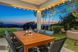 An outdoor dining area with a wooden table and chairs, string lights, and a view of the landscape.