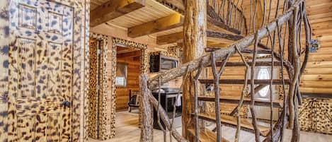 A spiral staircase with a rustic design, wooden walls with a leopard print pattern, and a kitchen area in the background.