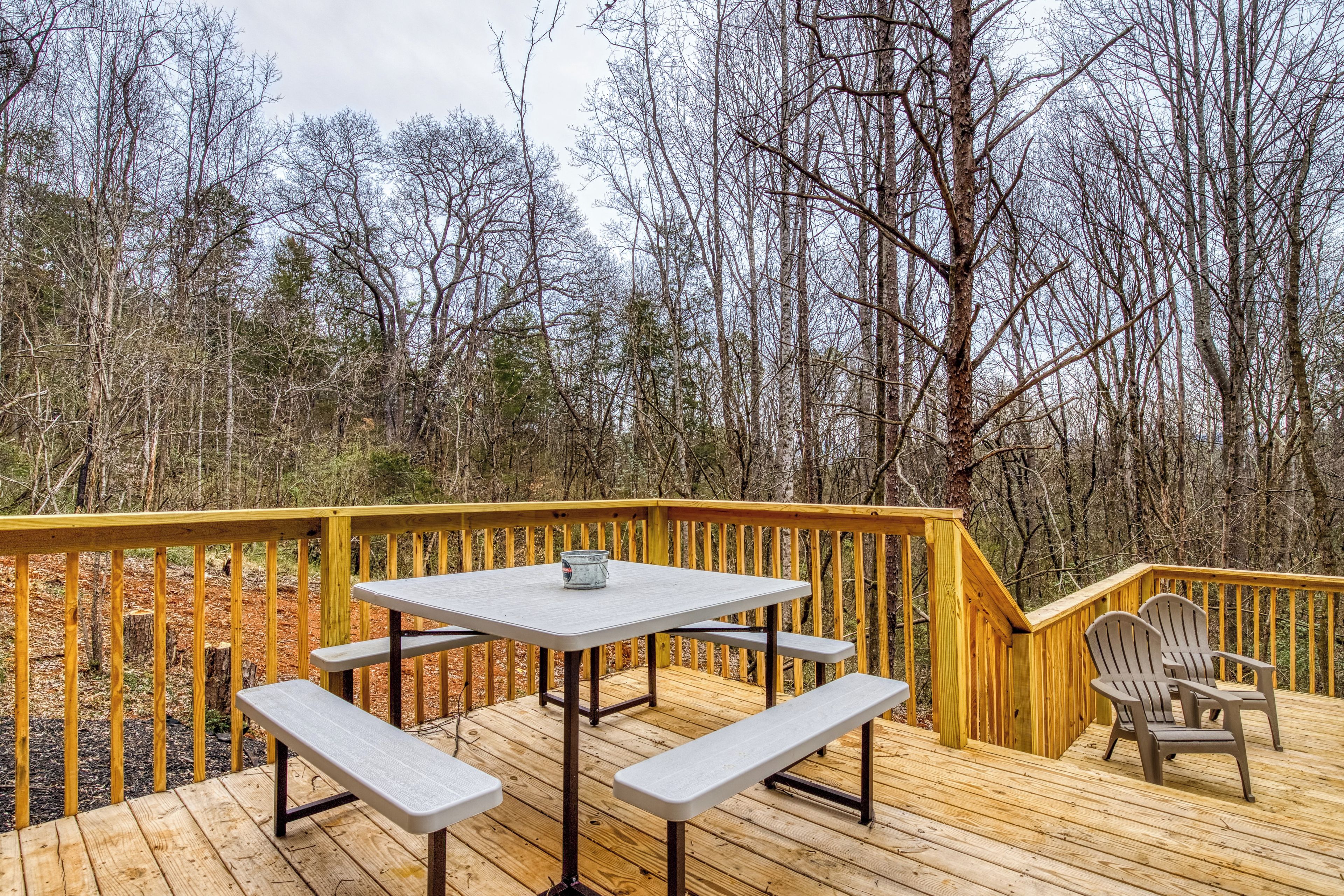 A wooden deck with a picnic table and benches, surrounded by trees.