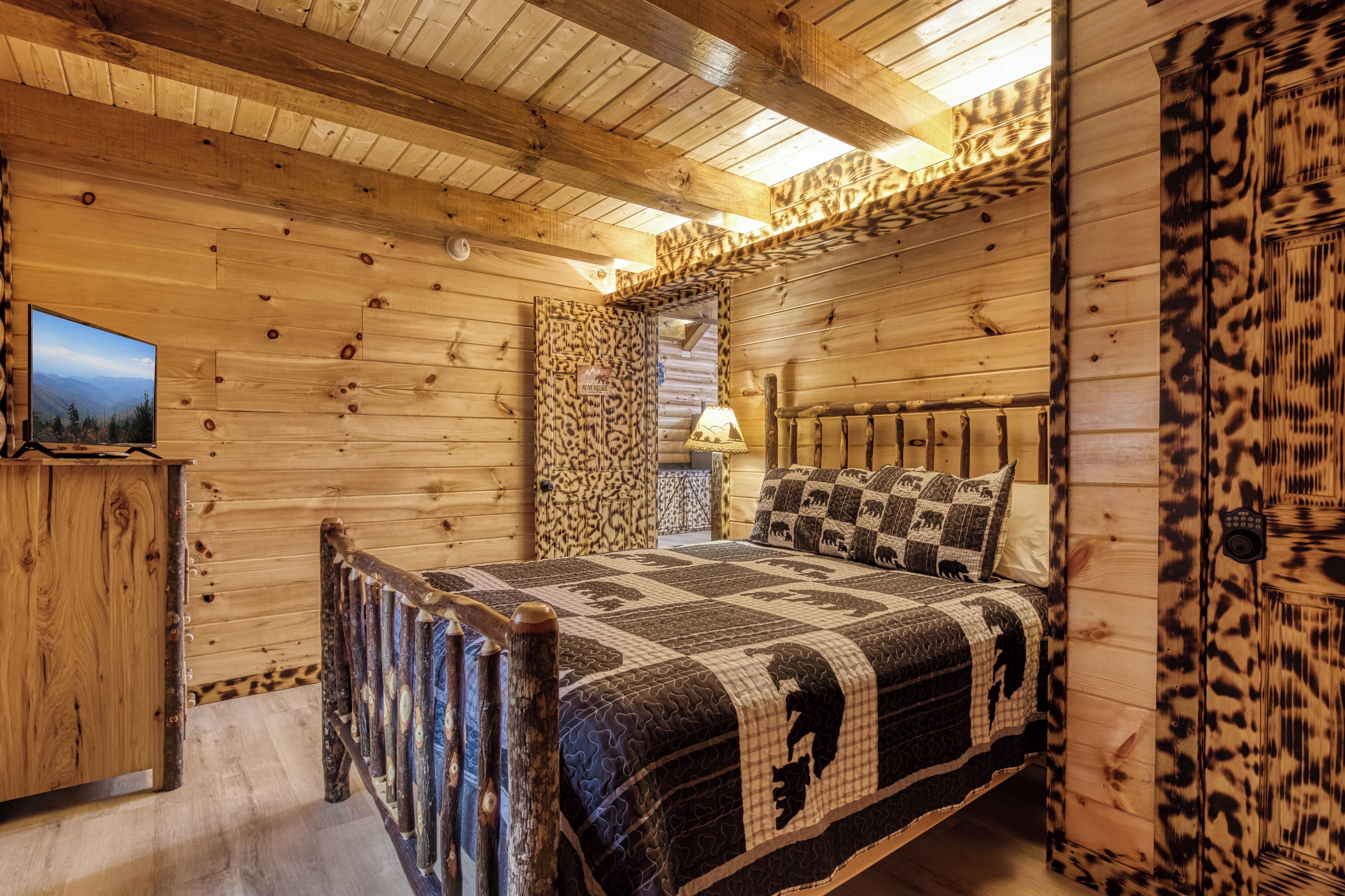 Interior de uma cabana de madeira com cama, televisão e porta com o letreiro 'Wild & Wooly'.