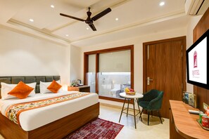 Quarto de hotel com cama, escrivaninha, cadeira, ventilador de teto e janela com vista para o banheiro.