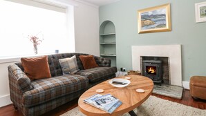 Ein Wohnzimmer mit einem karierten Sofa, einem runden Couchtisch, einem Kamin und einem Gemälde an der Wand.