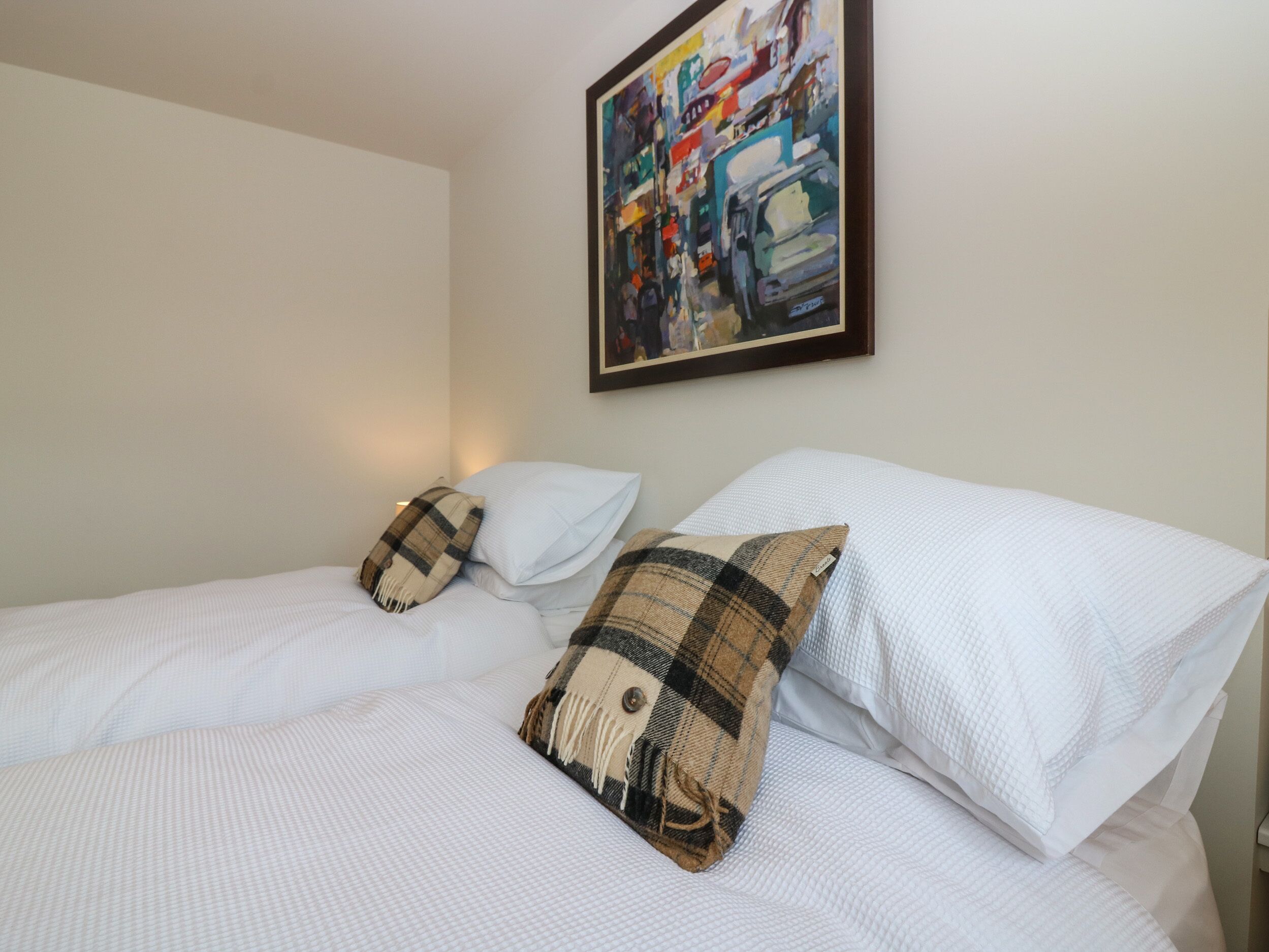A neatly made bed with white bedding and two plaid pillows.