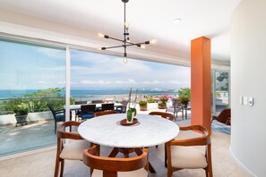 Una mesa redonda con sillas, una lámpara colgante y vista al mar.