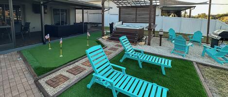 A backyard with artificial grass, a hot tub, and outdoor seating.