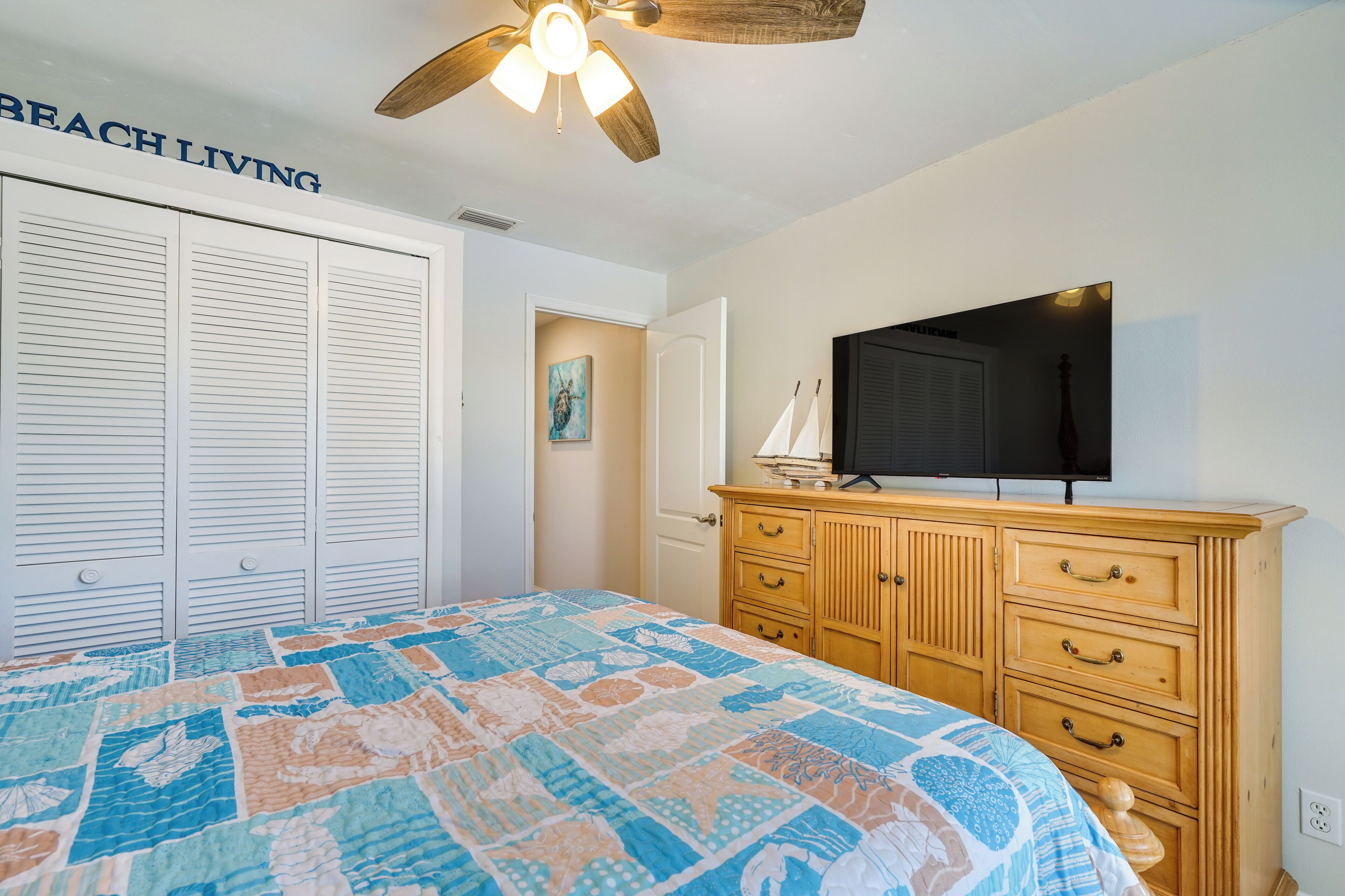 A bedroom with a bed, a wooden dresser, a ceiling fan, and a television on the dresser.