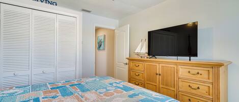 A bedroom with a bed, a wooden dresser, a ceiling fan, and a television on the dresser.
