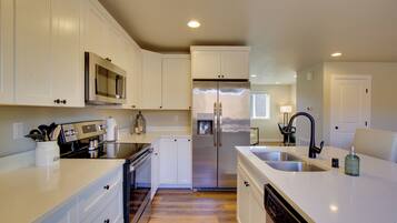 A modern kitchen with white cabinetry, stainless steel appliances, and a large island with a sink.