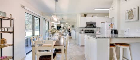 A modern kitchen with white cabinets, a granite countertop, and a dining area with a wooden table and chairs.