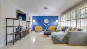 A living room with a blue brick wall, a gray sofa, yellow armchairs, a coffee table, and a bookshelf.