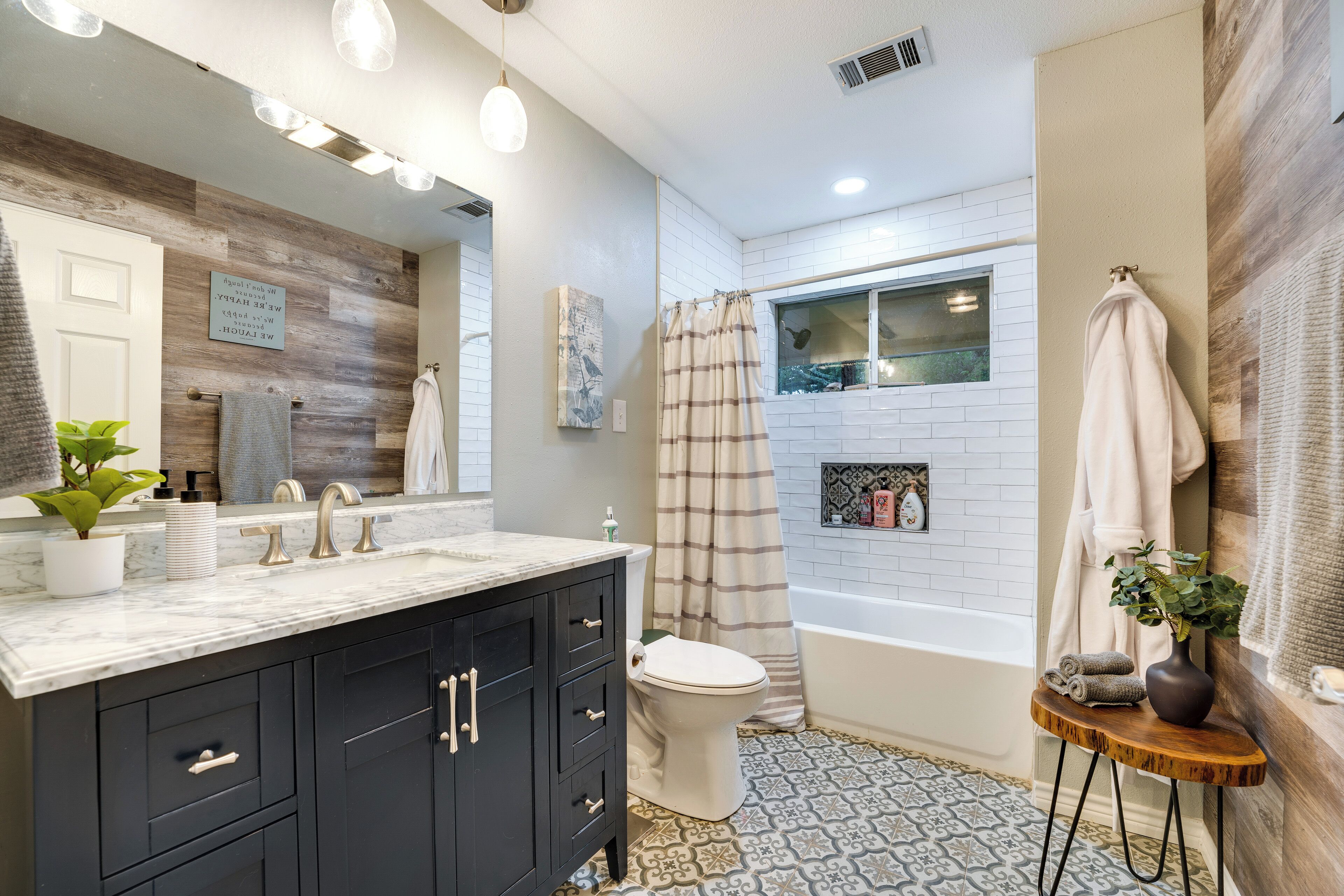 A modern bathroom with a wooden vanity, a white toilet, a bathtub, and a shower curtain.