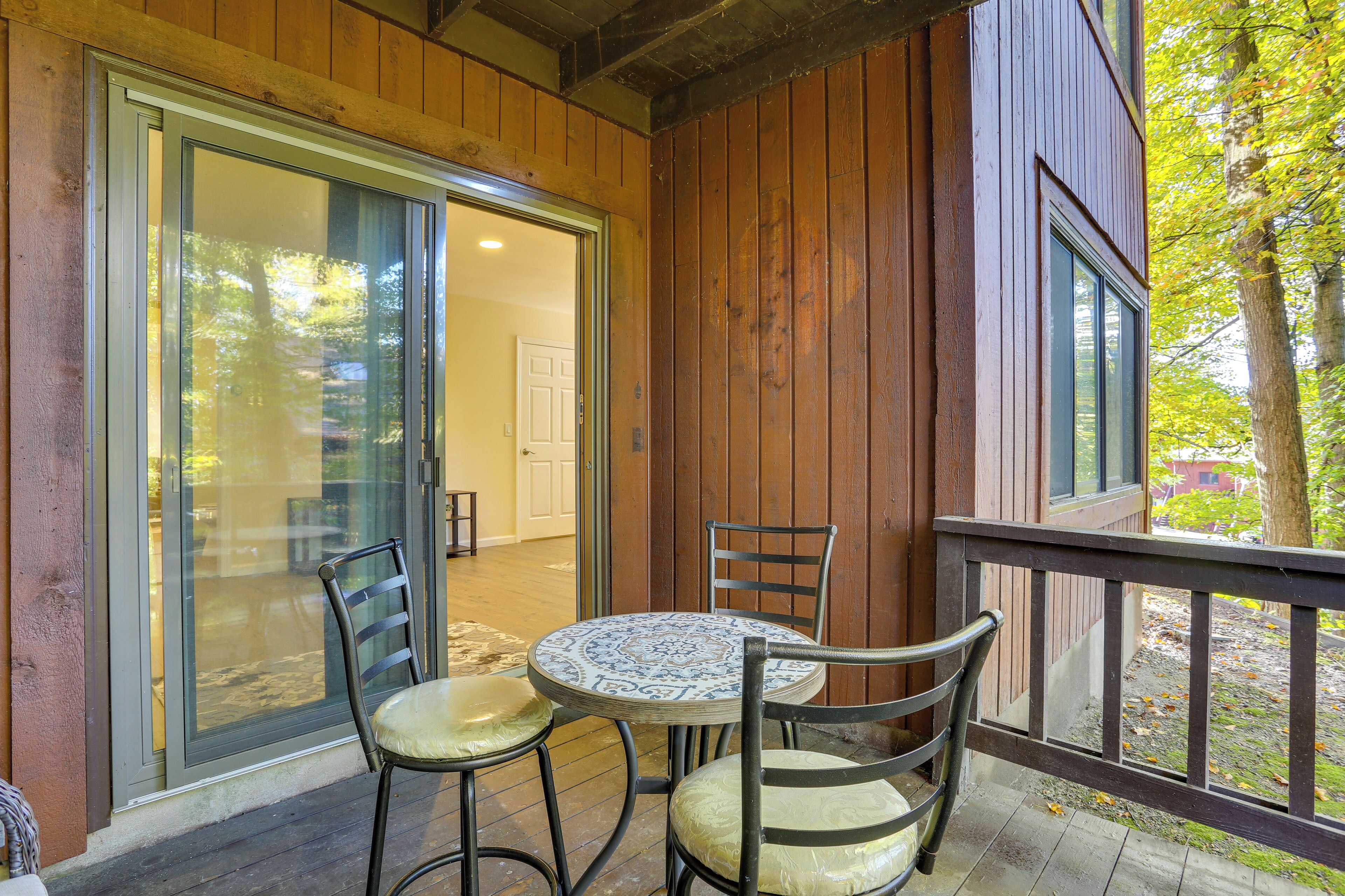 A wooden deck with a glass door leading to a room, two chairs, and a small round table.