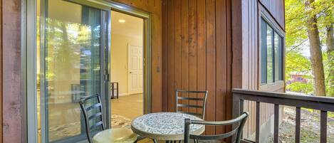 A wooden deck with a glass door leading to a room, two chairs, and a small round table.