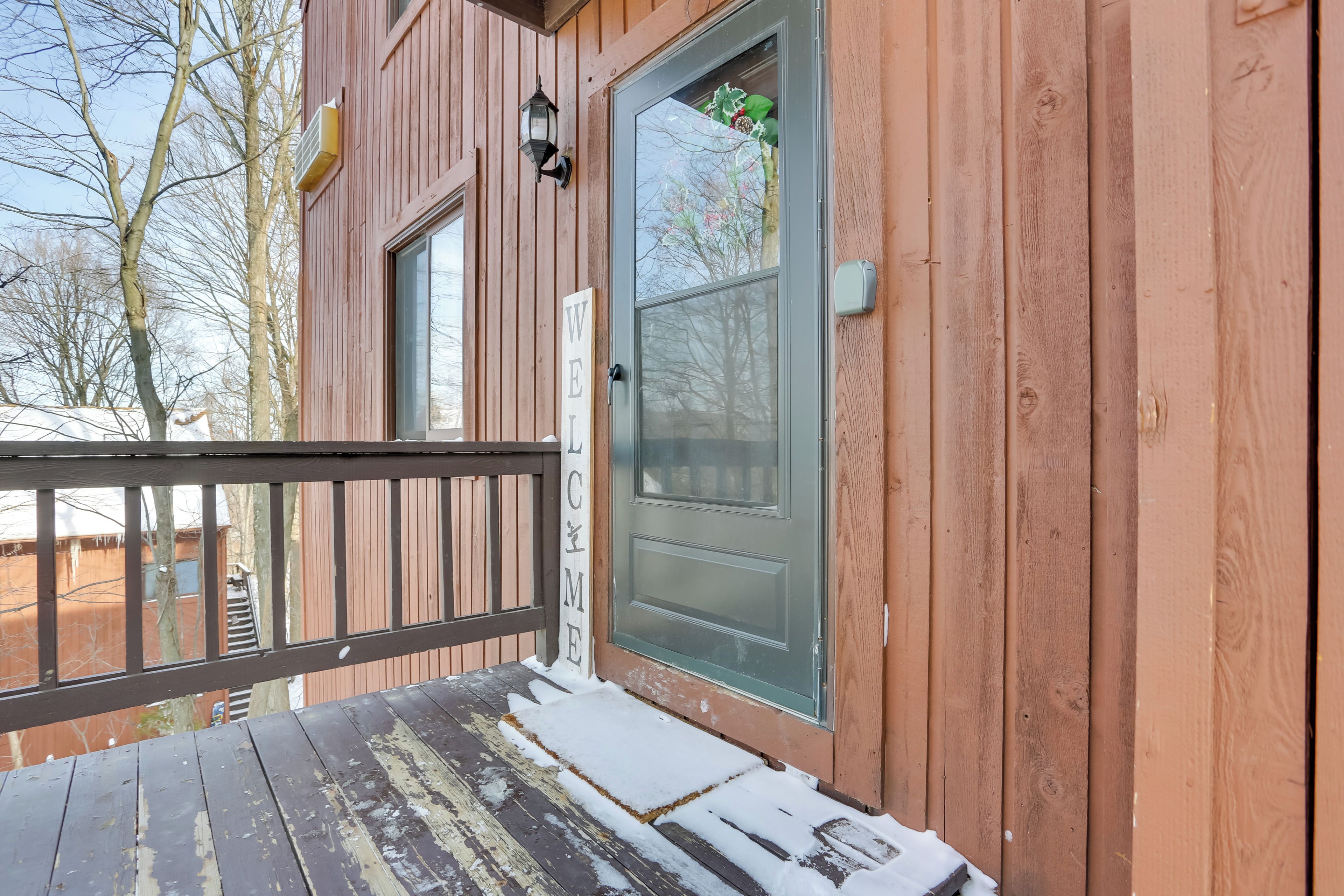 Une cabane en bois avec un porche, une porte dotée d’un panneau en verre dépoli et une pancarte indiquant « BIENVENUE ».