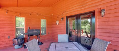 An outdoor patio with a wooden table and chairs, a grill, and string lights.