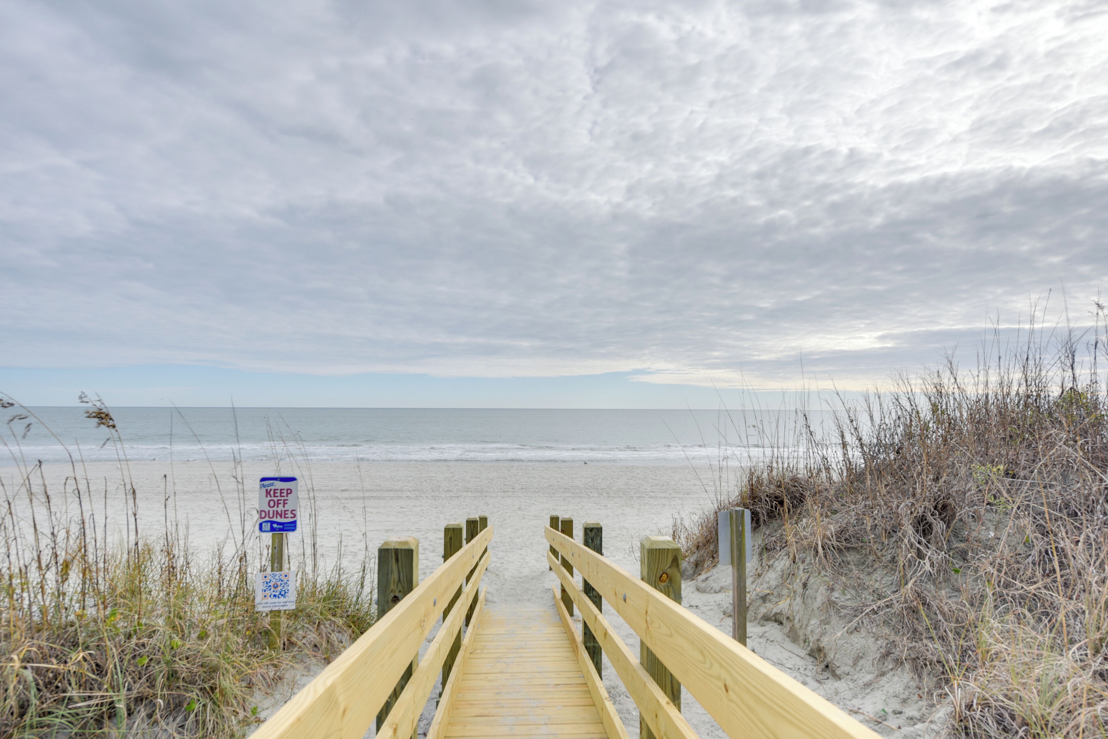 A wooden boardwalk leading to a beach with a sign that reads "KEEP OFF DUNES."