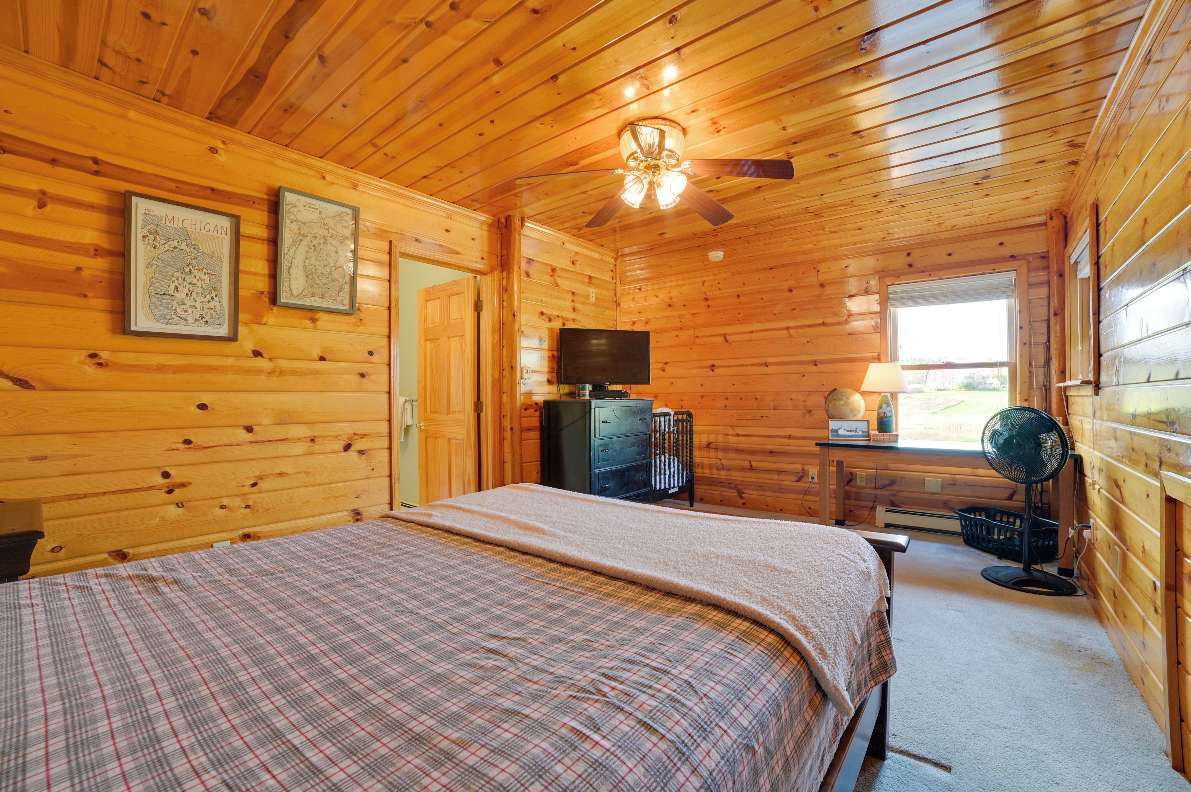 A wooden cabin room with a bed, a television, a fan, and a window.