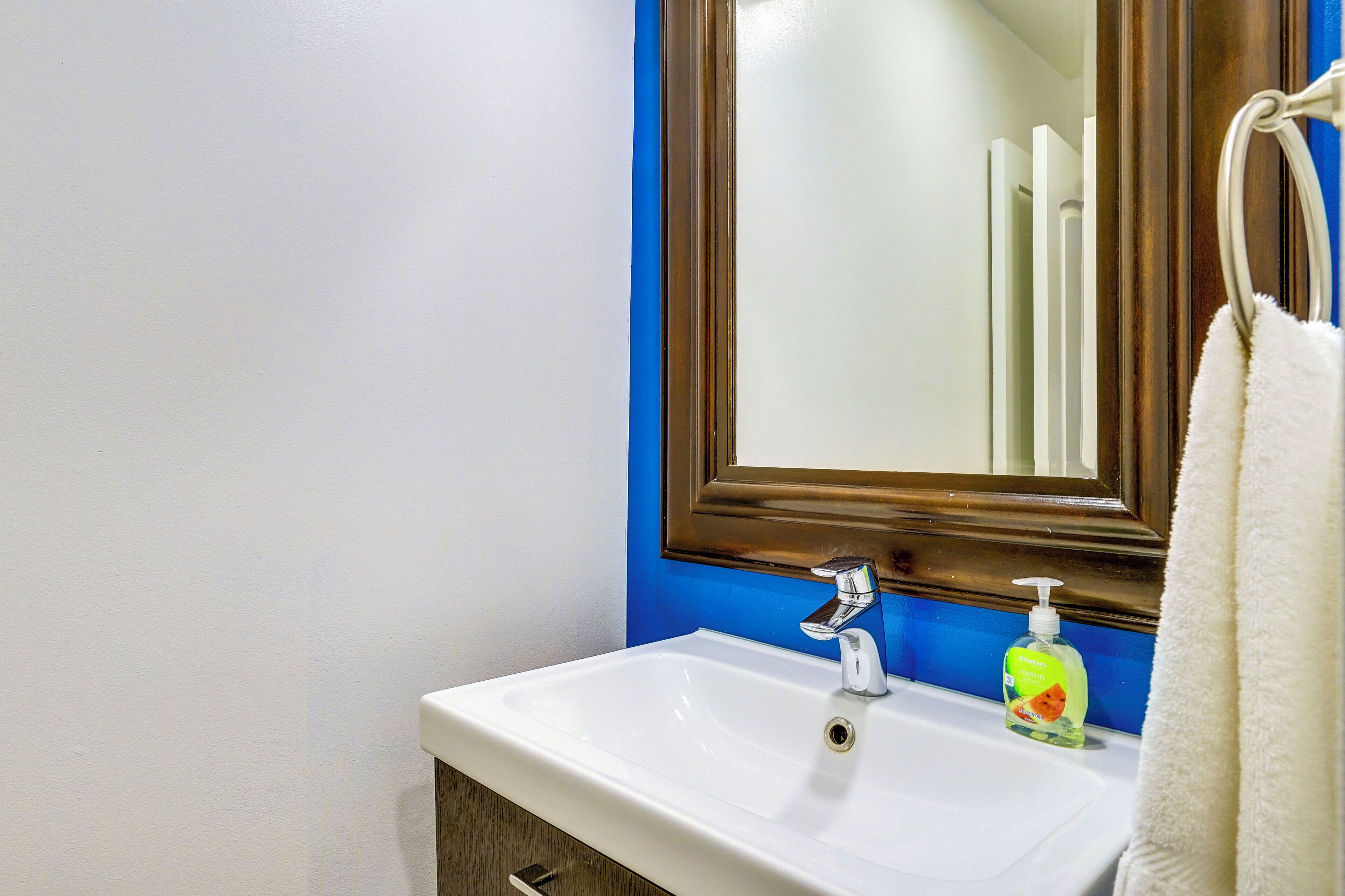 A bathroom with a white sink, a blue wall, and a wooden-framed mirror.