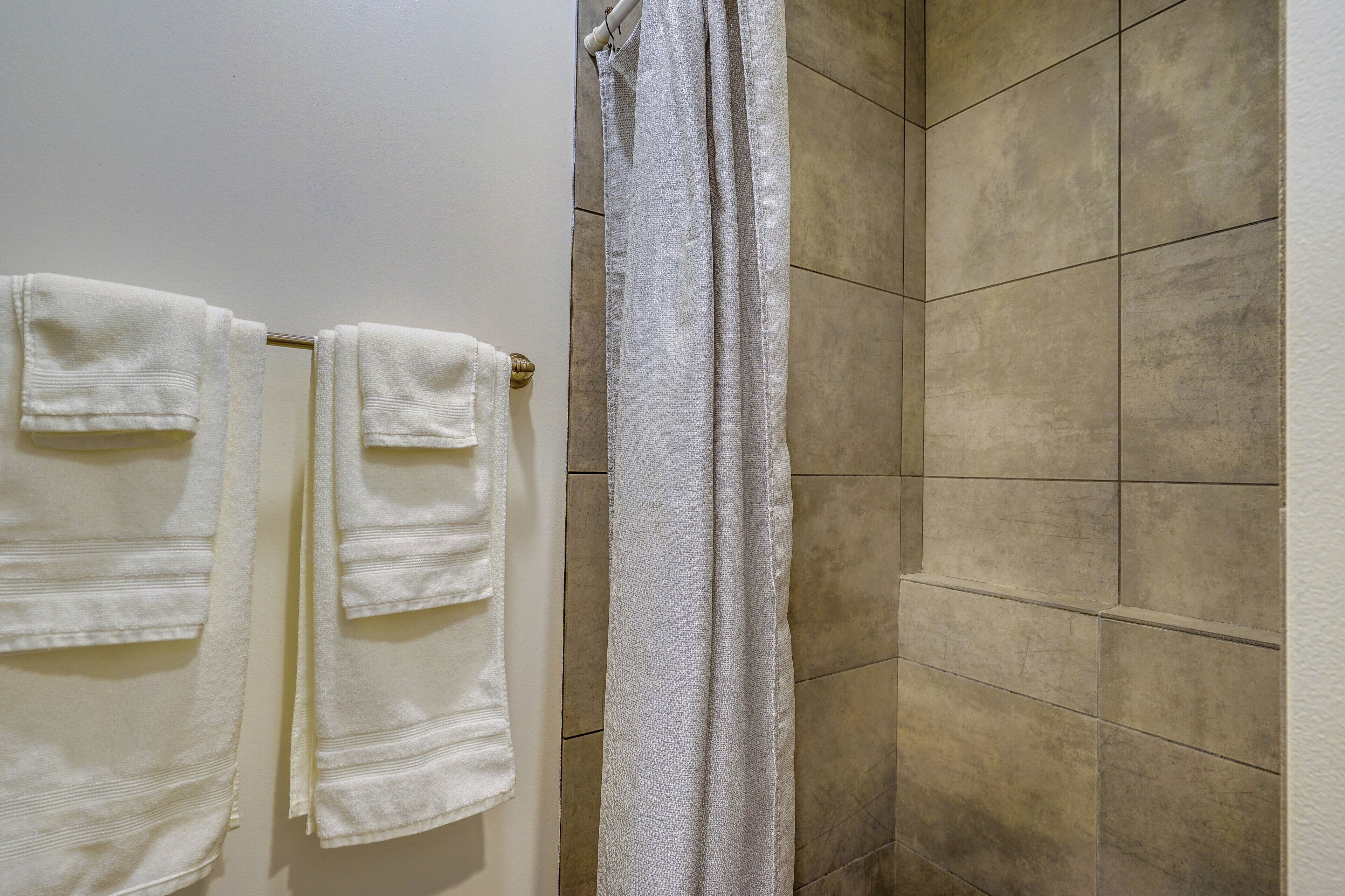 Un baño con baldosas color crema, un perchero blanco con dos toallas y una cortina de ducha blanca.