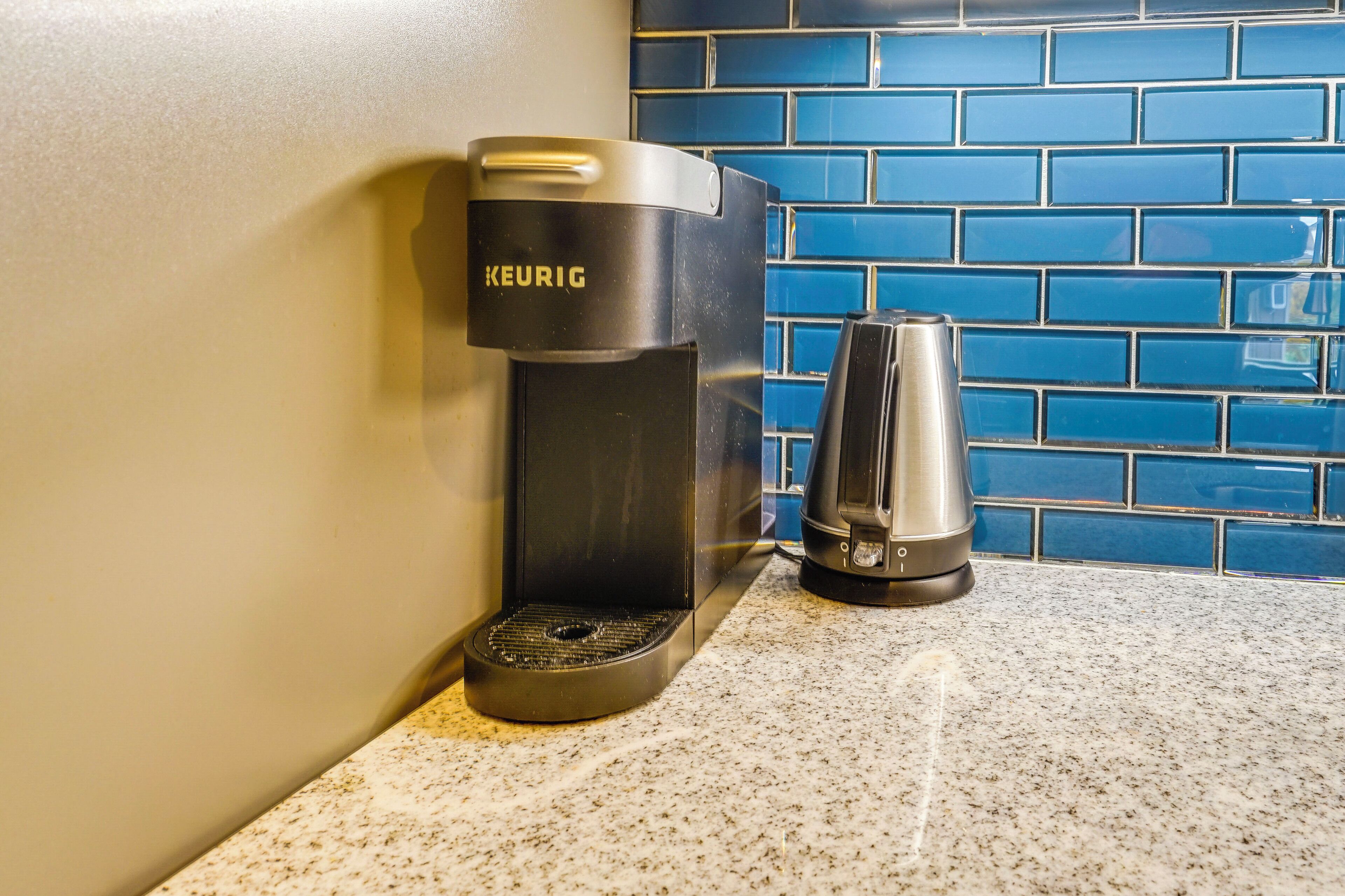 A Keurig coffee maker and a coffee pot on a kitchen counter with blue-tiled backsplash.
