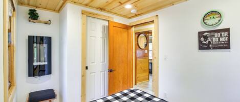 A bedroom with a checkered bedspread, a wooden ceiling, a wall clock, a motivational quote, and a mirror.