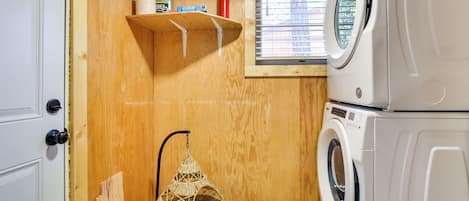 Une petite buanderie comprenant un lave-linge, un étendoir et une petite étagère où sont rangés les produits de nettoyage.