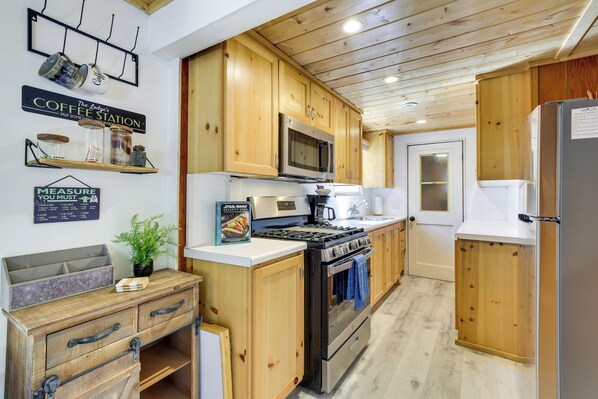 A kitchen with wooden cabinets, a stove, microwave, and a refrigerator. There are signs on the wall, including one that says "Coffee Station." - Sugarloaf Vacation Rental ~ 7 Mi to Big Bear Lake! (Sugarloaf)