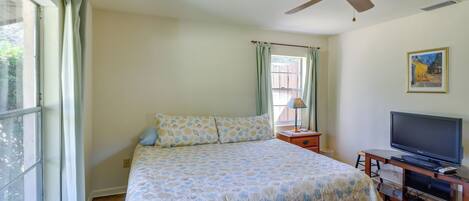 Quarto com cama, ventoinha no teto, televisão e janela com cortinas.