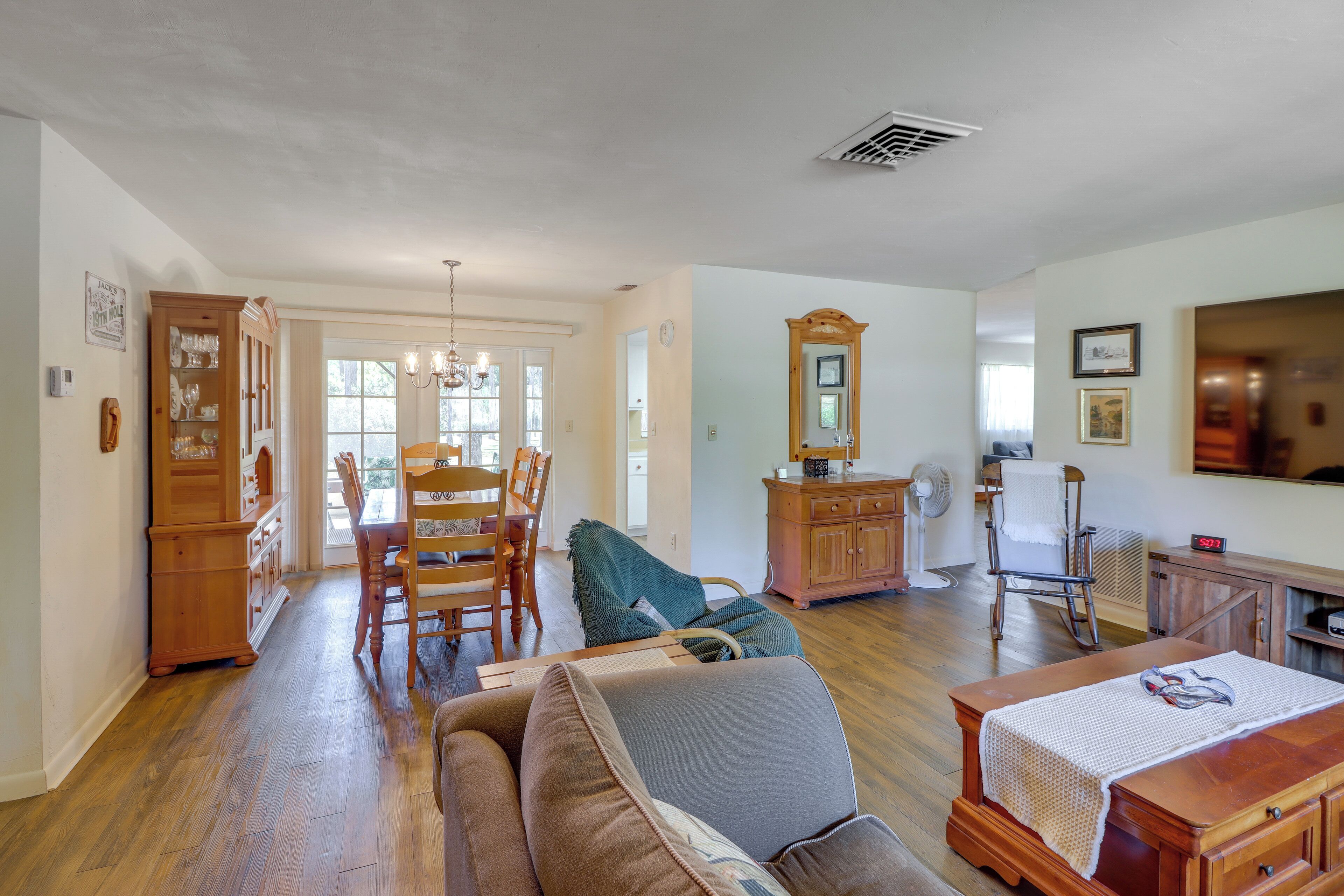 A spacious living room with hardwood floors, a dining area with wooden furniture, and a large mirror on the wall.
