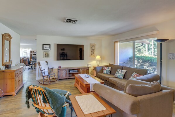 A spacious living room with a large TV, comfortable seating, a wooden dining table, and a view through large windows. - 2 Mi to Rainbow River: Home in Dunnellon (Dunnellon)