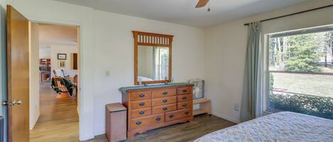 Une chambre avec une commode en bois, un ventilateur de plafond, un grand lit et une vue sur l’extérieur par une fenêtre.