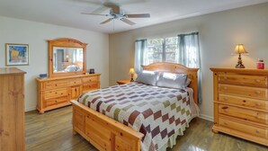 A bedroom with a wooden bed, a nightstand with a lamp, a dresser, a ceiling fan, and a window with curtains. - 2 Mi to Rainbow River: Home in Dunnellon (Dunnellon)