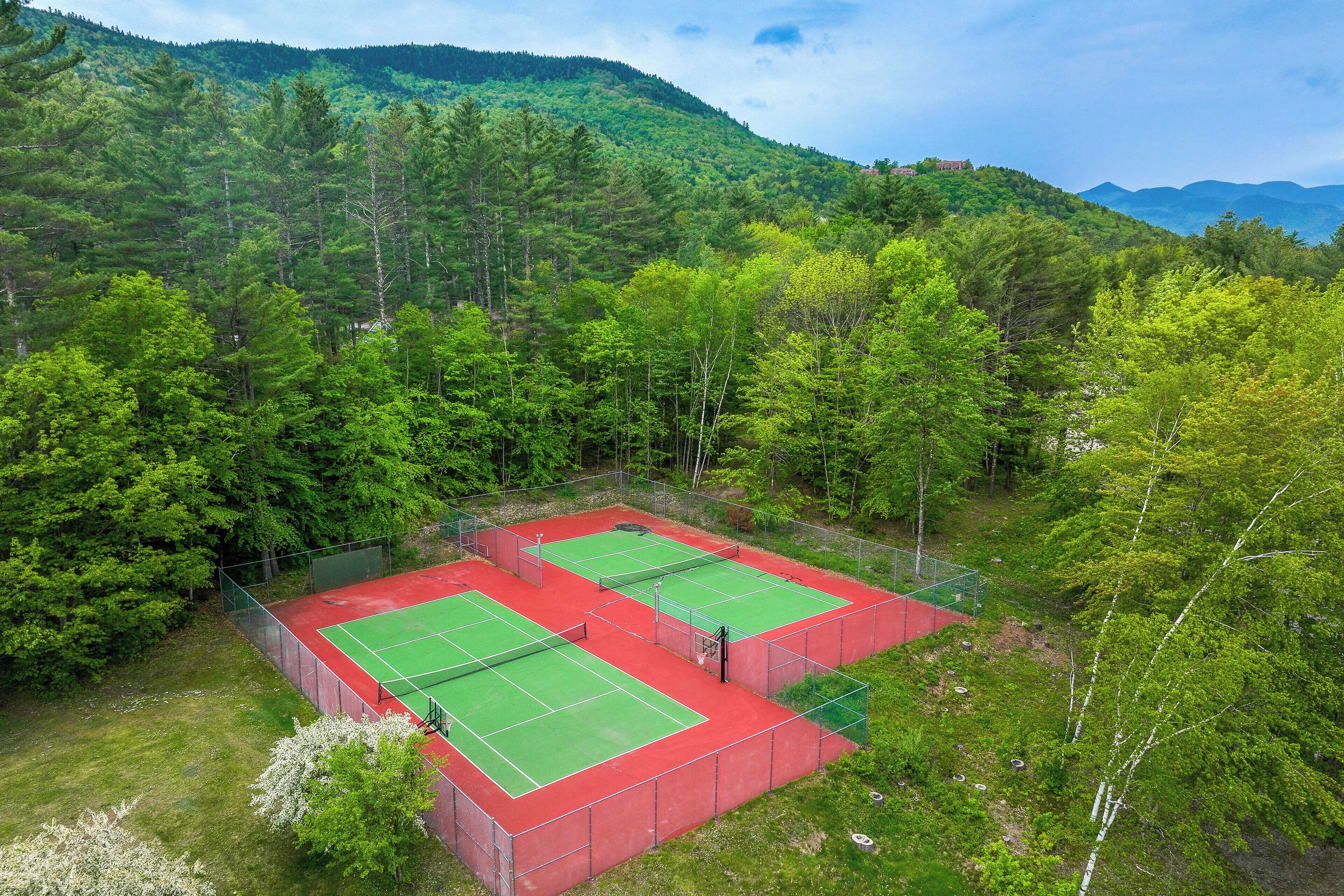 An outdoor tennis court surrounded by dense forest and mountains.