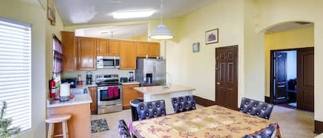 A kitchen with wooden cabinets, a microwave, and a refrigerator. There is a dining table with chairs and a bar stool.