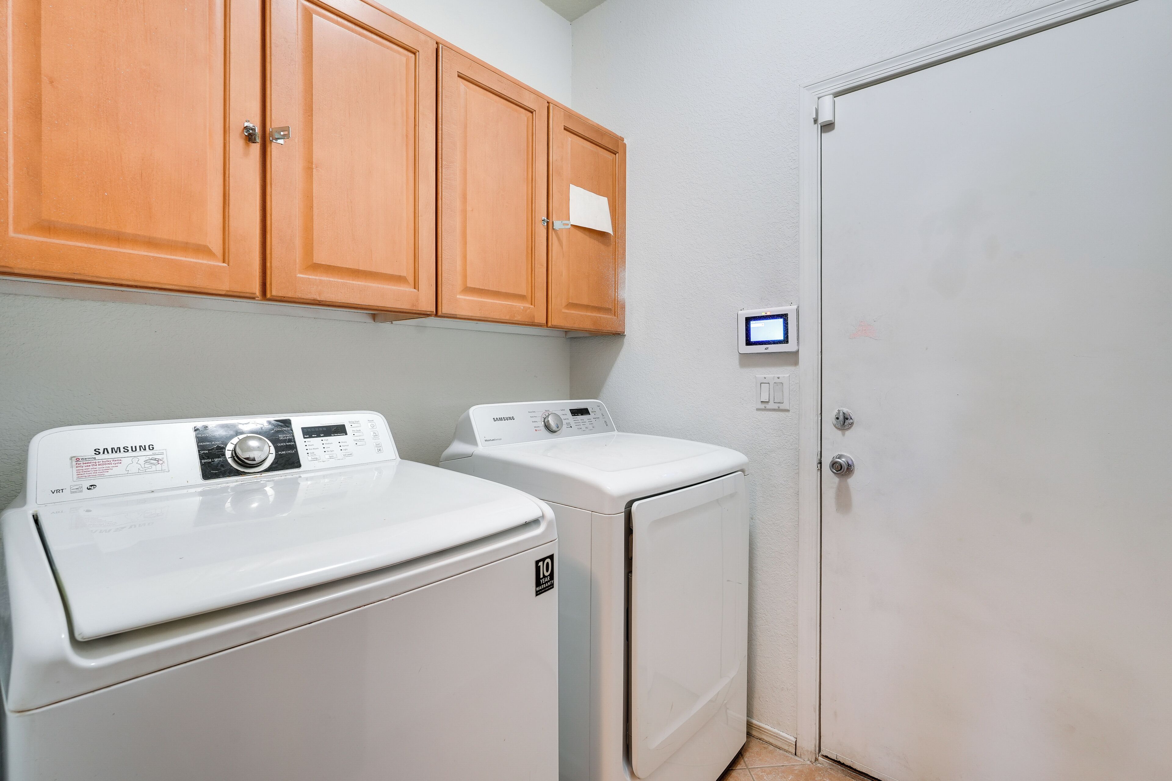 A laundry room with two white washers and dryers, wooden cabinets, and a white door.