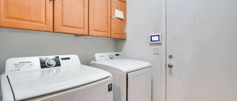 A laundry room with two white washers and dryers, wooden cabinets, and a white door.